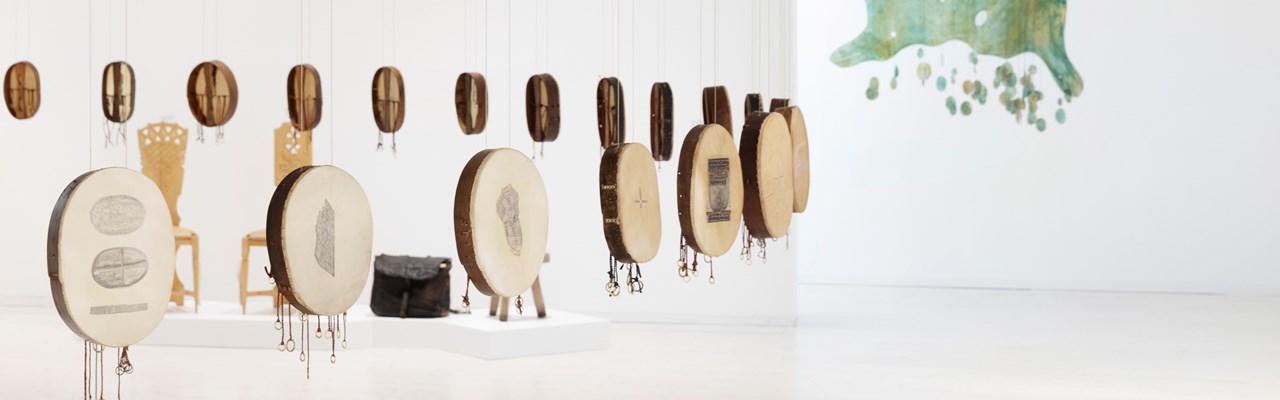 Verk i en konstutställning, en cirkel av samiska trummor och en fritt hängande bemålad älghud med tenn och pärlbroderi.